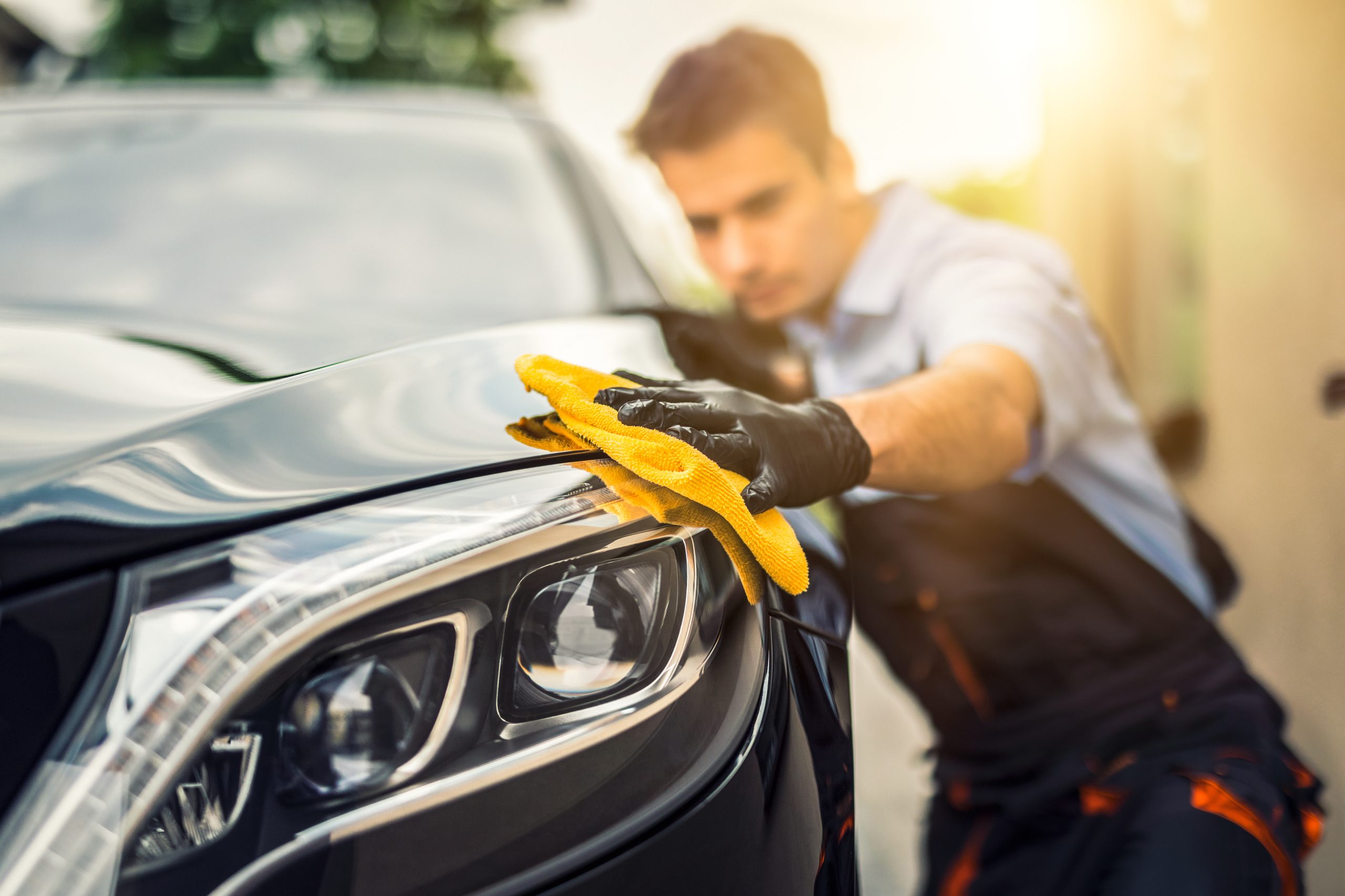 man using a yellow microfiber towel to polish and buff a black mercedes benz